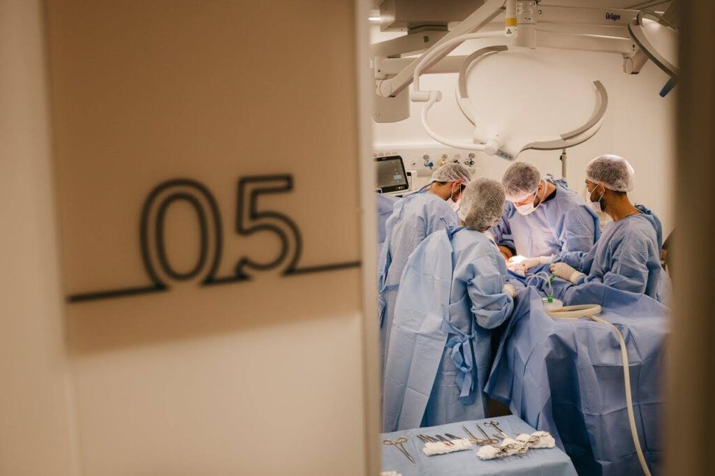 Four surgeons in surgical attire skillfully operate a patient in a hospital room labelled 05, with precision instruments neatly arranged on the table.