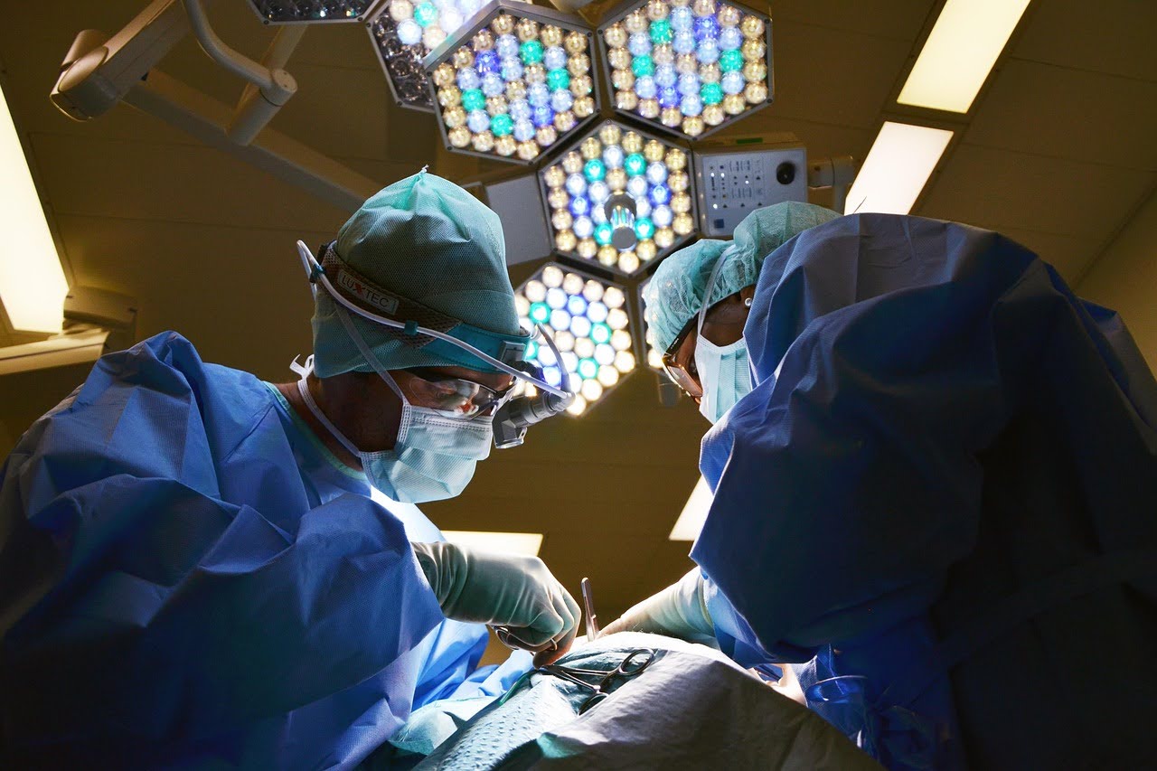 A close-up of two surgeons in medical attire performing surgery on different areas of a patient's body.