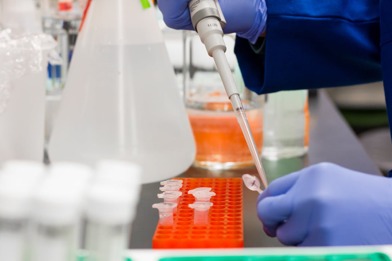 Scientist using a pipette to transfer liquid samples into test tubes during a biochemistry experiment.