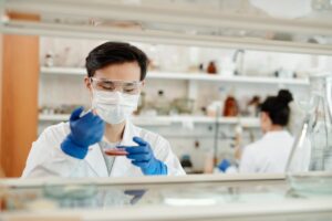Biochemist wearing protective gear examines a petri dish with samples inside a modern laboratory.