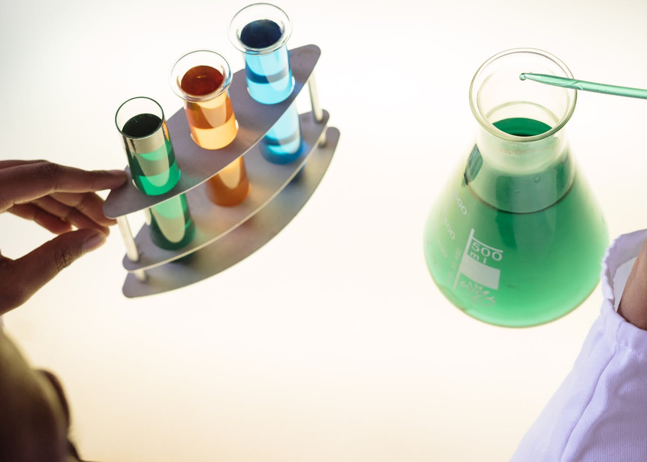 Scientist handling colourful chemical solutions in test tubes and a green liquid-filled flask during a biochemistry experiment.