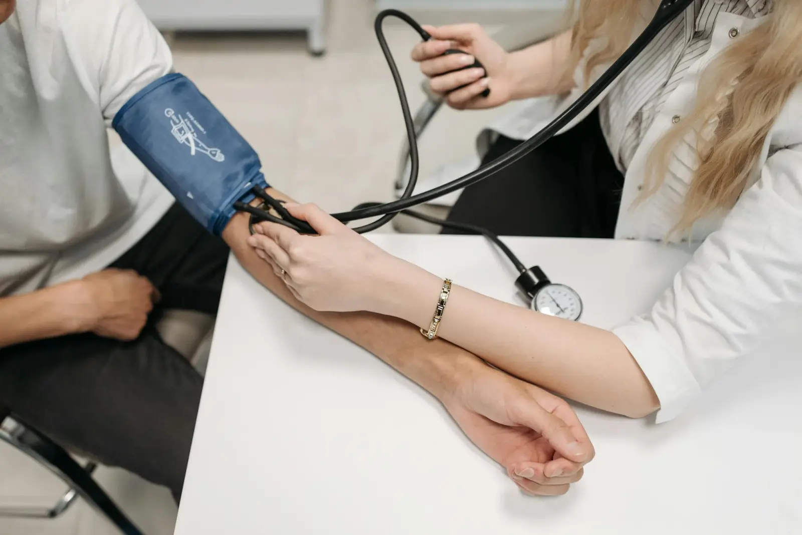 Medical professional checking a patient's blood pressure with a manual sphygmomanometer in a clinic setting.
