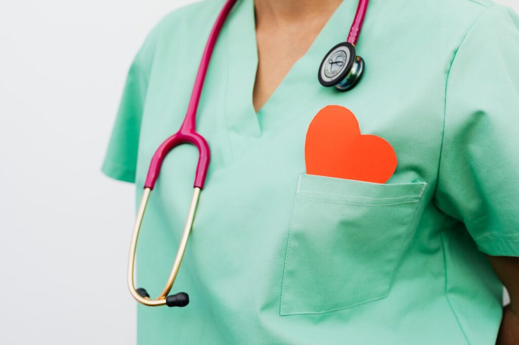 Healthcare professional wearing green scrubs and a stethoscope with a red heart symbol in the pocket, representing cardiology care.