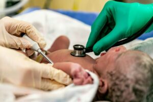 Medical professionals examining a newborn baby using a stethoscope and thermometer in a neonatal care unit.