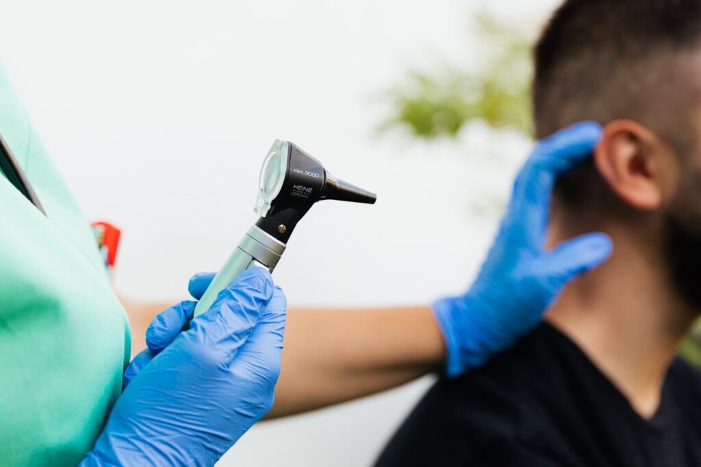 Healthcare provider holding an otoscope during an ear examination with the patient seated nearby.