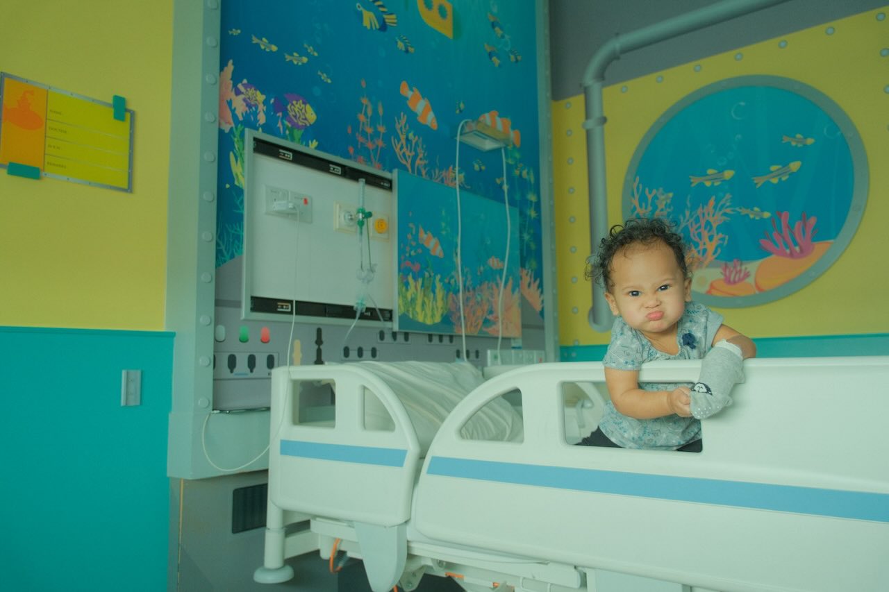 Toddler in a colourful paediatric hospital room receiving care for an arm injury