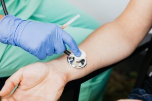Doctor in gloves checking a patient’s pulse using a stethoscope during a cardiovascular examination.