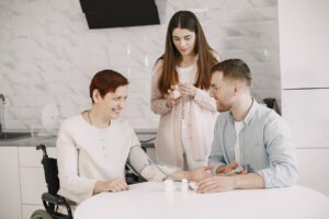 A family medicine doctor checking the blood pressure of a senior woman in a wheelchair, with a caregiver assisting at home.