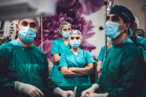 Group of general surgeons in green scrubs and masks standing attentively in an operating theatre, preparing for surgery.