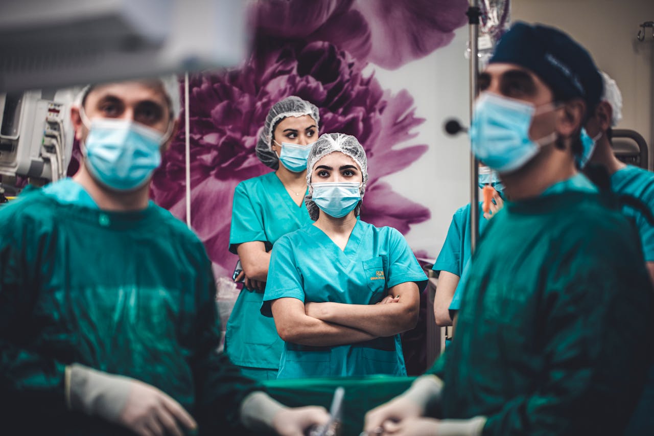 Group of general surgeons in green scrubs and masks standing attentively in an operating theatre, preparing for surgery.