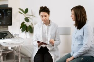A gynaecologist reviews medical notes while speaking with a pregnant woman during a prenatal consultation in a clinic.