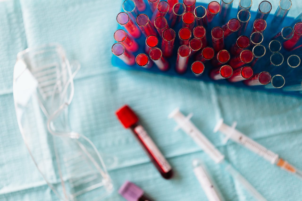 Collection of red-filled test tubes and syringes arranged on a blue medical tray in a clinical setting.