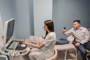 An obstetrician performing an ultrasound scan on a pregnant woman while her partner records the moment.