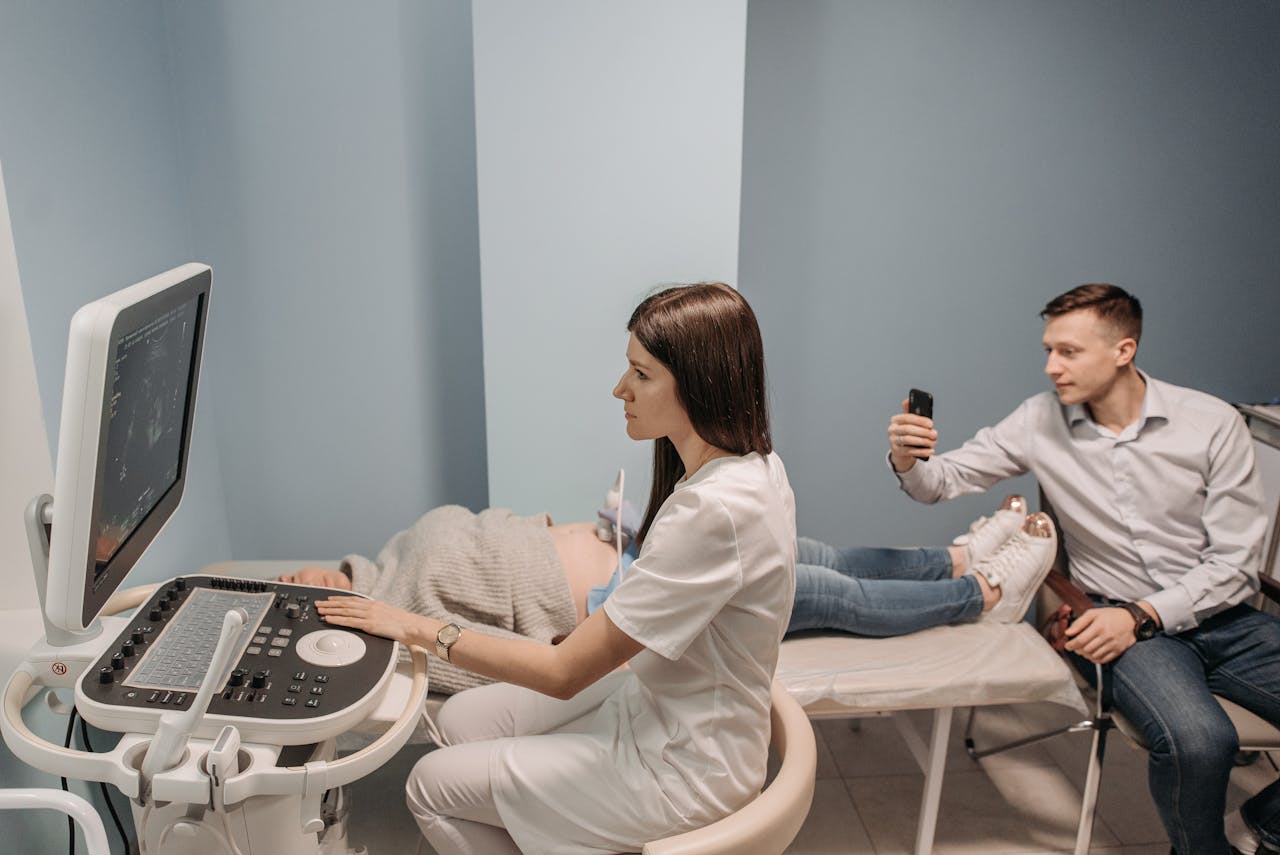 An obstetrician performing an ultrasound scan on a pregnant woman while her partner records the moment.