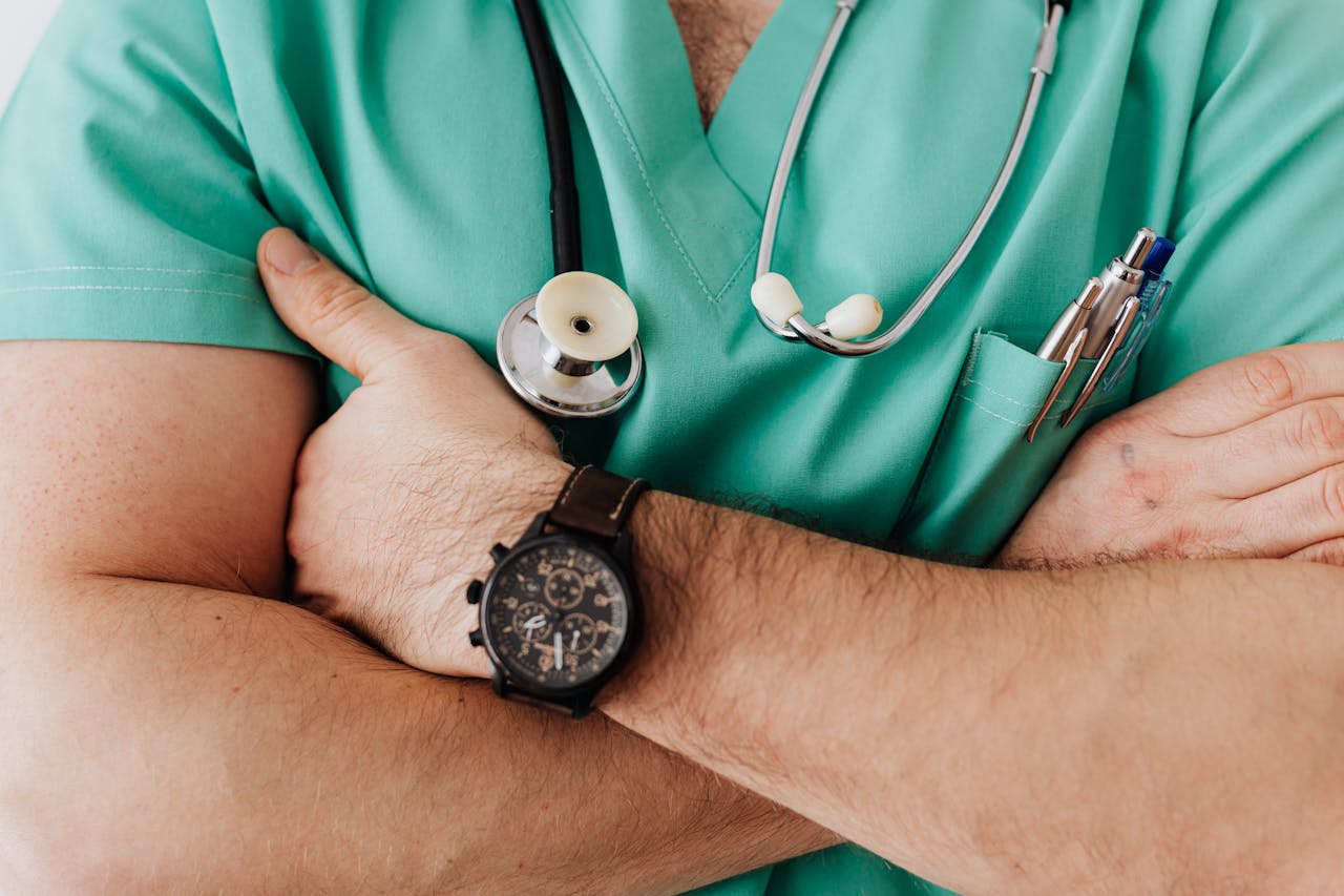 Close-up of a confident doctor in green medical scrubs with arms crossed and a stethoscope around the neck.