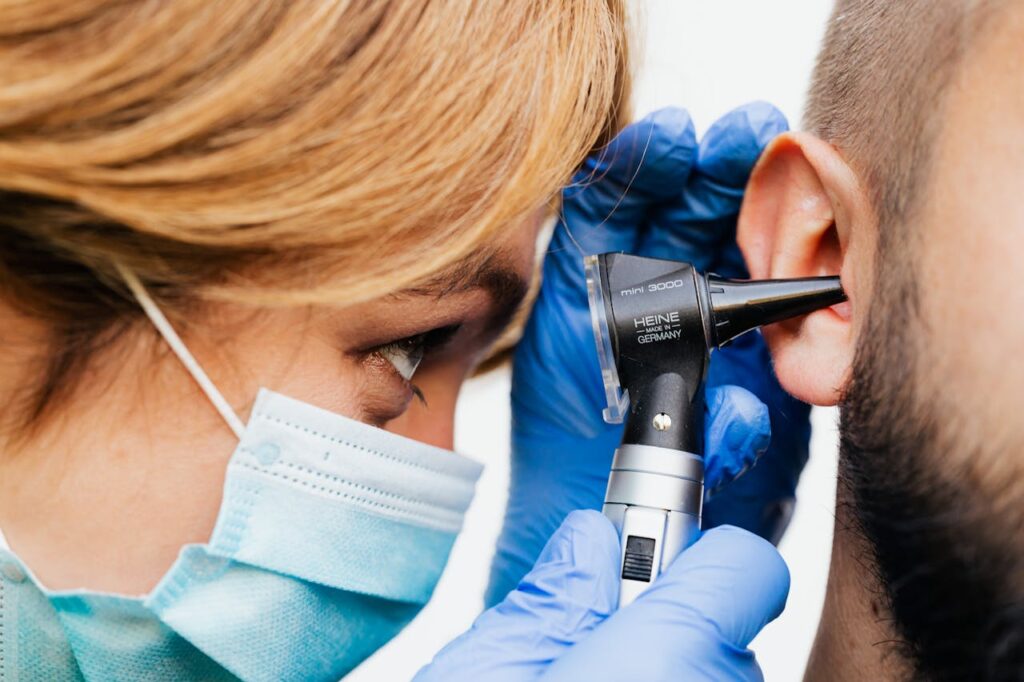 Medical professional wearing a mask and gloves inspecting a patient’s ear canal with an otoscope.