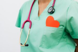 Healthcare professional wearing green scrubs and a stethoscope with a red heart symbol in the pocket, representing cardiology care.