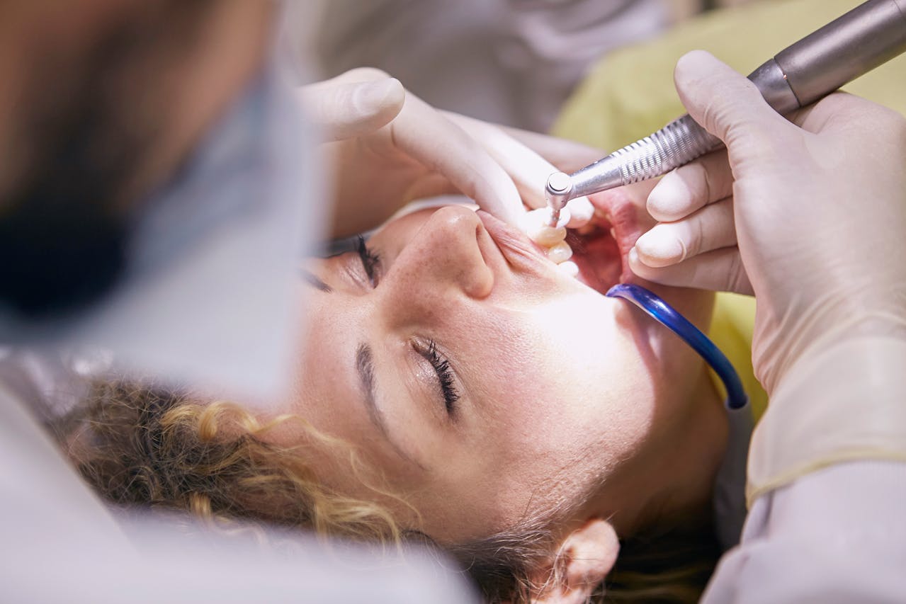 Dental professional using a dental drill to perform a restorative procedure on a patient's teeth during a clinical treatment session.