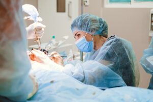 A female general surgeon wearing a surgical mask and cap performs a delicate procedure in a sterile operating room.