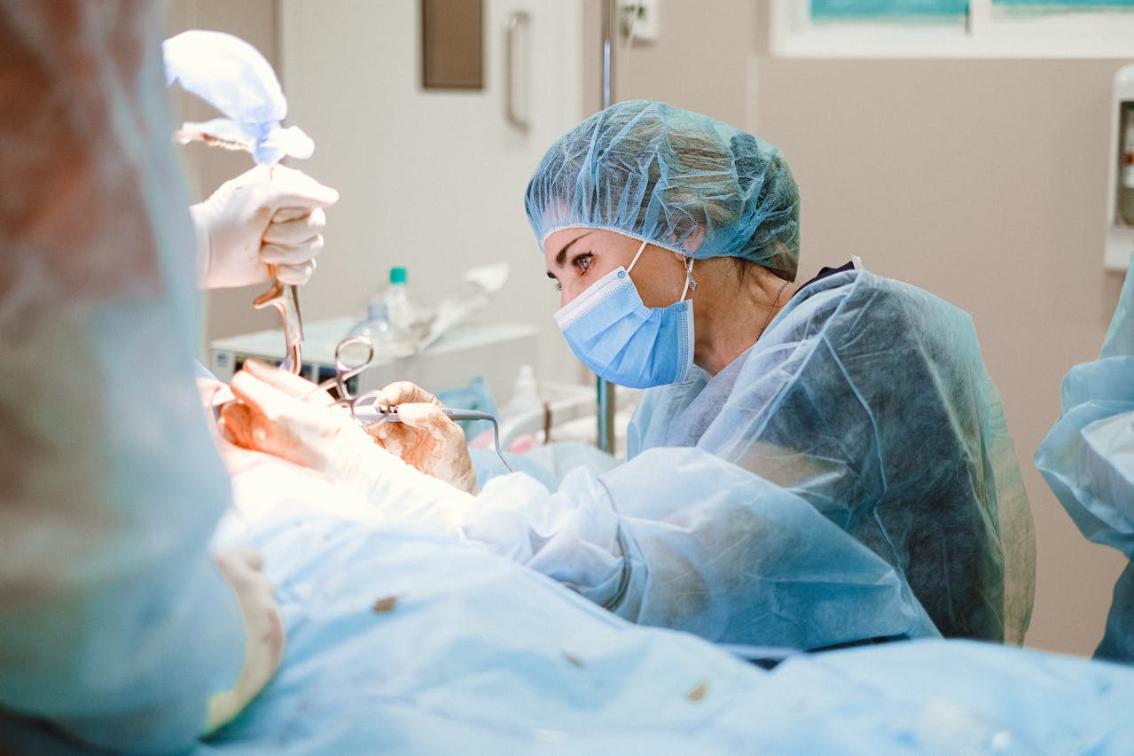 A female general surgeon wearing a surgical mask and cap performs a delicate procedure in a sterile operating room.